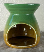 Back of a glossy green ombre into yellow and brown ceramic wax warmer with a wide top bowl and an open back, photographed against a light textured wall and gray surface.