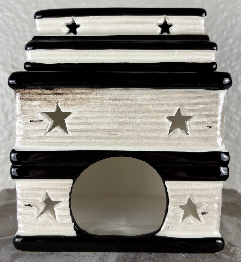 A small ceramic wax warmer with a tiered stack of books showing the pages with star cutouts, and a round entrance hole, shown against a neutral textured background.