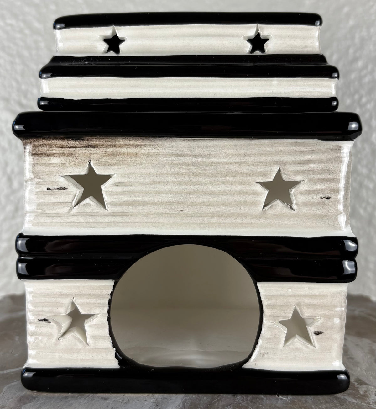 A small ceramic wax warmer with a tiered stack of books showing the pages with star cutouts, and a round entrance hole, shown against a neutral textured background.
