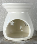 Back of a glossy white ceramic wax warmer with a wide top bowl and an open back, photographed against a light textured wall and gray surface.