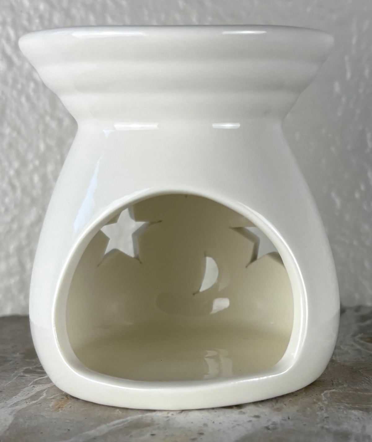 Back of a glossy white ceramic wax warmer with a wide top bowl and an open back, photographed against a light textured wall and gray surface.
